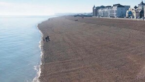 Ein weiter Sandstrand, bewölkter Himmel, einige Personen und Gebäude im Hintergrund.
