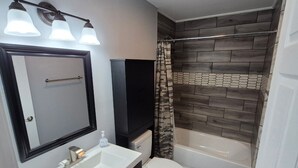A bathroom with a white sink, a mirror, a toilet, a bathtub, and a shower curtain. - New Modern Studio in Maryville (Maryville)