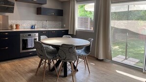 A modern kitchen with dark cabinets, a round dining table, and chairs, a large window with a view of greenery. - Charming air-conditioned house in a quiet area - Sospel (Sospel)