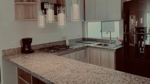 A modern kitchen with granite countertops, a black refrigerator, and wooden cabinets. - Luxury apartment in serena del mar (Cartagena)