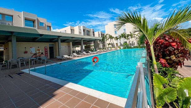 A swimming pool with lounge chairs and a palm tree. - Luxury apartment in serena del mar (Cartagena)
