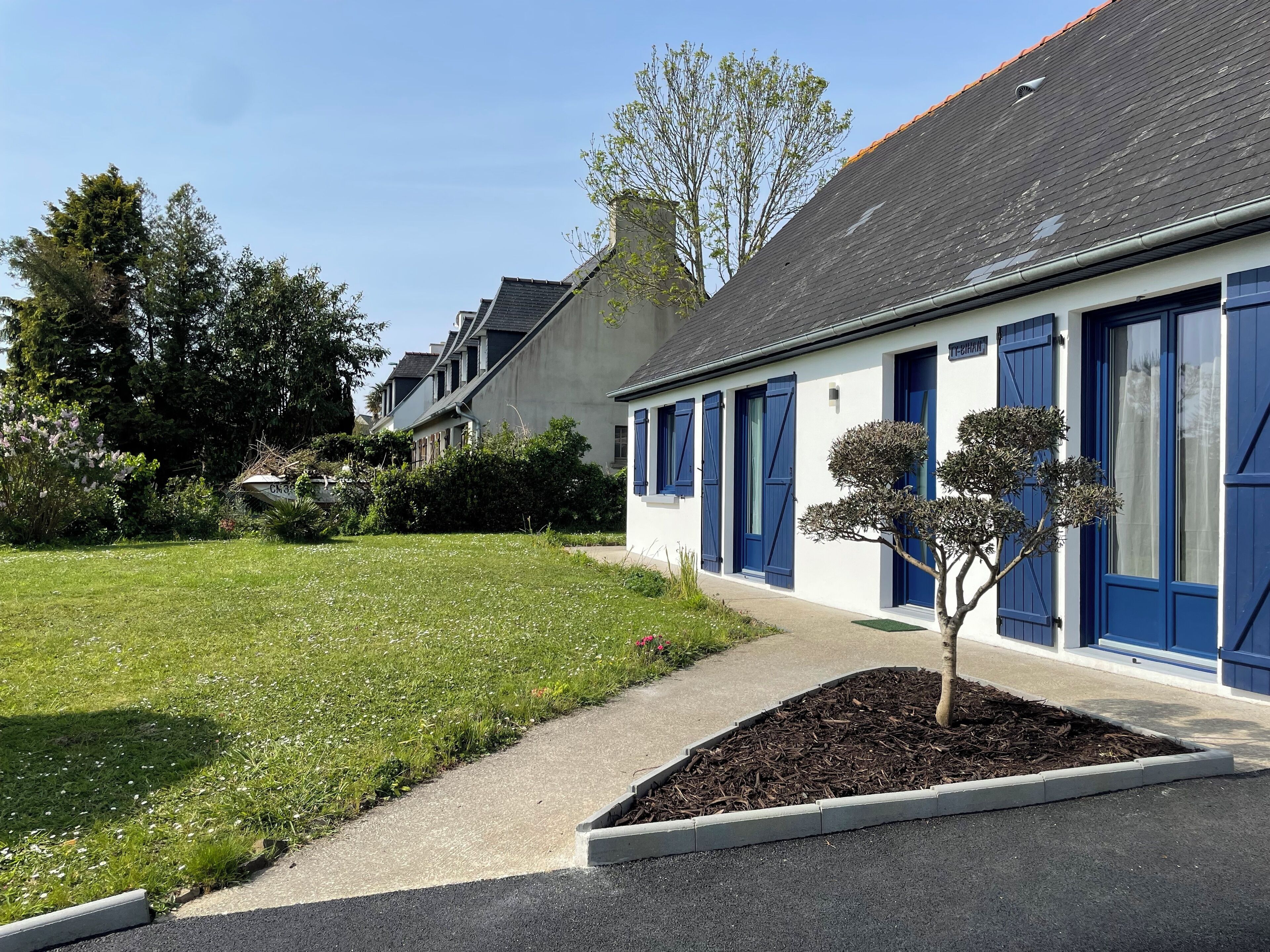 Ein Gebäude mit blauen Fensterläden, einem gepflegten Rasen und einem kleinen Baum im Vordergrund.