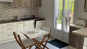 A modern kitchen with a dining area, featuring a white table and chairs, wooden cabinets, and a hanging light fixture. - TY BIHAN ☀️ (Crozon)