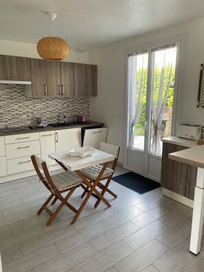 A modern kitchen with a dining area, featuring a white table and chairs, wooden cabinets, and a hanging light fixture. - TY BIHAN ☀️ (Crozon)
