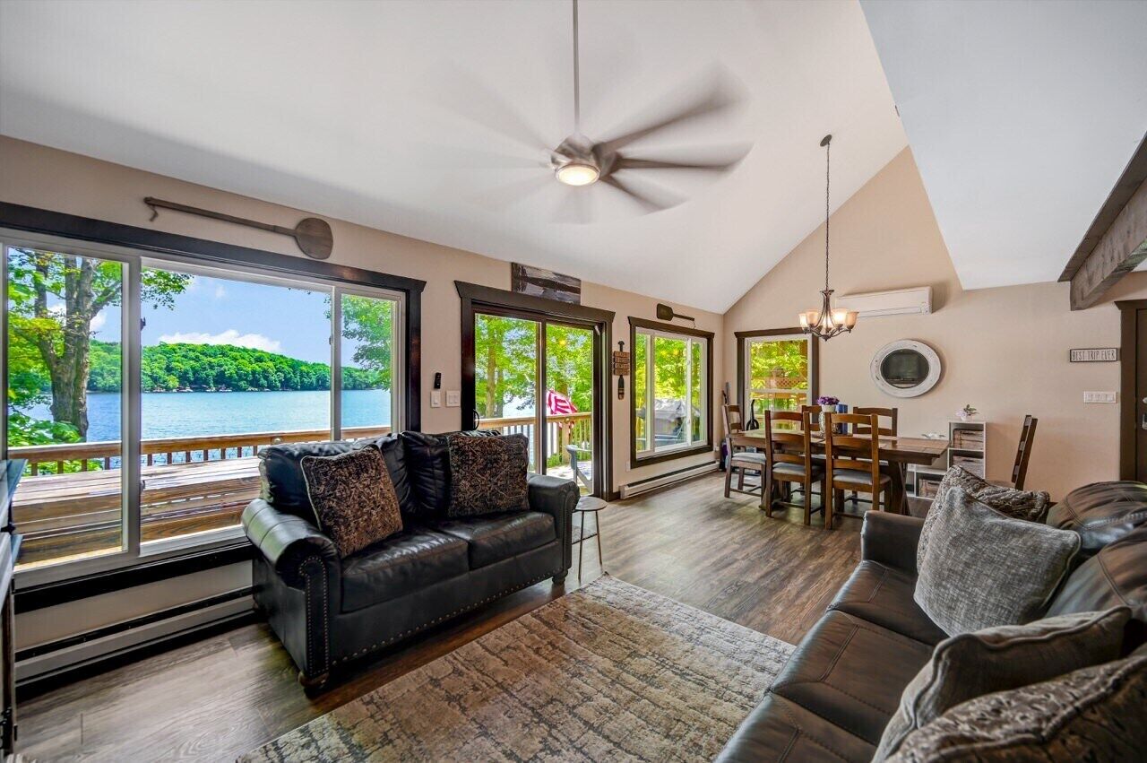 A spacious living room with a large window, a ceiling fan, a dining area, and a view of a lake.