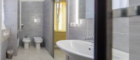 Un baño moderno con azulejos grises, un lavamanos blanco y dos inodoros.