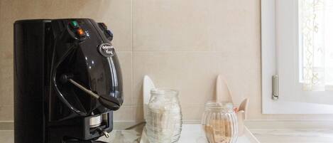 A kitchen with a coffee maker, a jar, and a window with a curtain.