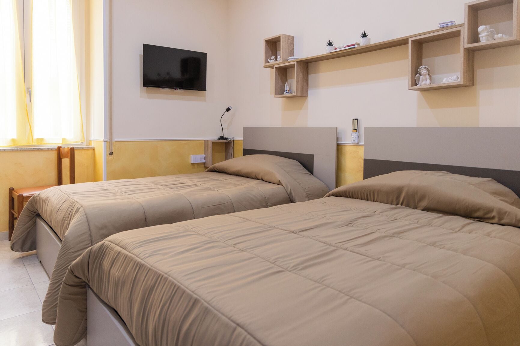 Zwei Betten mit passenden Kopfteilen, ein Flachbildfernseher an der Wand und ein Nachttisch mit einer Lampe.