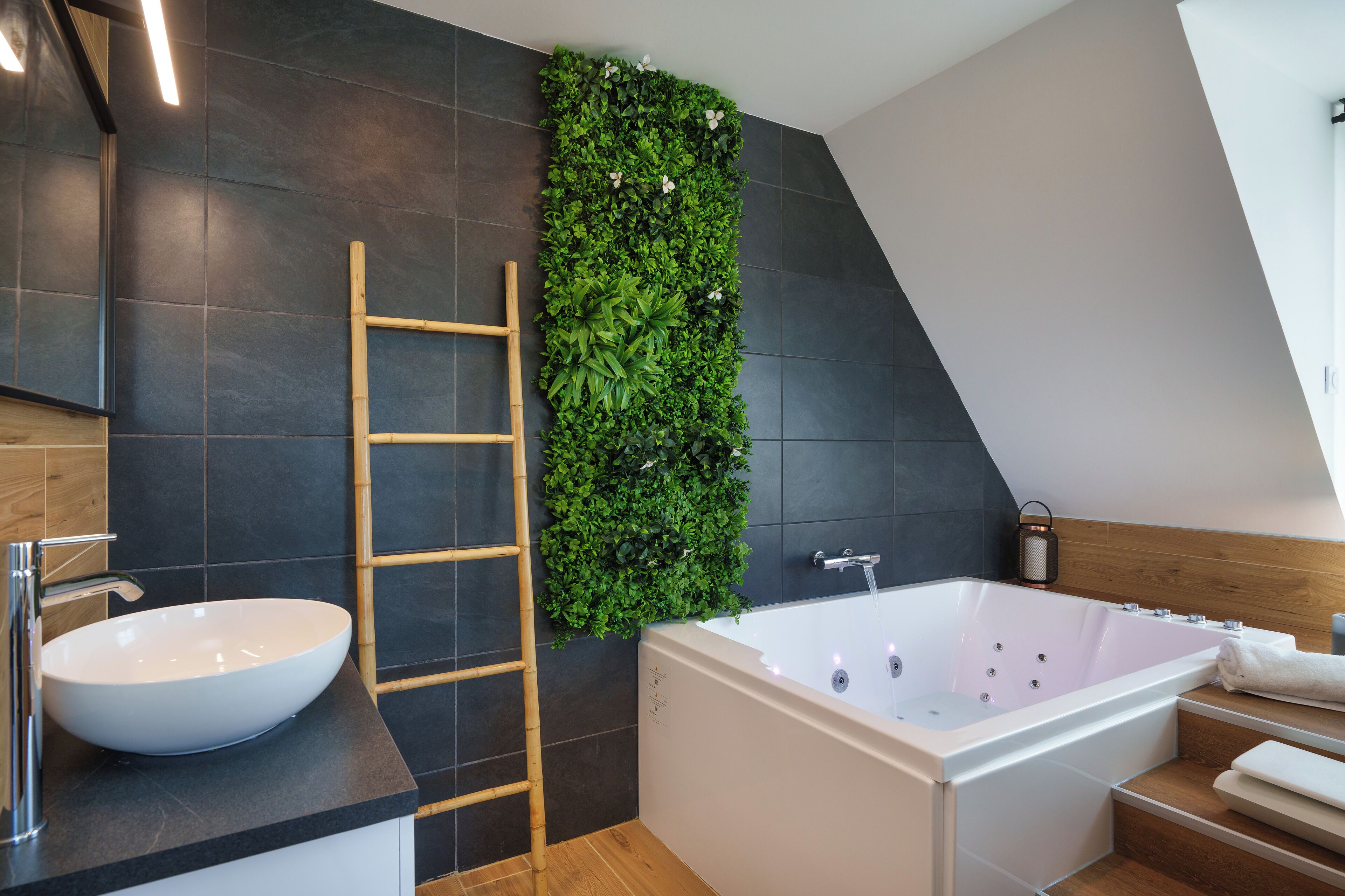 A modern bathroom with a white bathtub, a wooden ladder, and a green vertical garden.