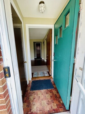 A hallway with a welcome mat, a door with a peephole, and a brick wall. - Comfortable 3BR House Near UB, Parking, WiFi, Backyard (Buffalo)