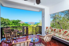 Ein Balkon mit Meerblick, Korbmöbel und eine Couch mit floralem Bezug.