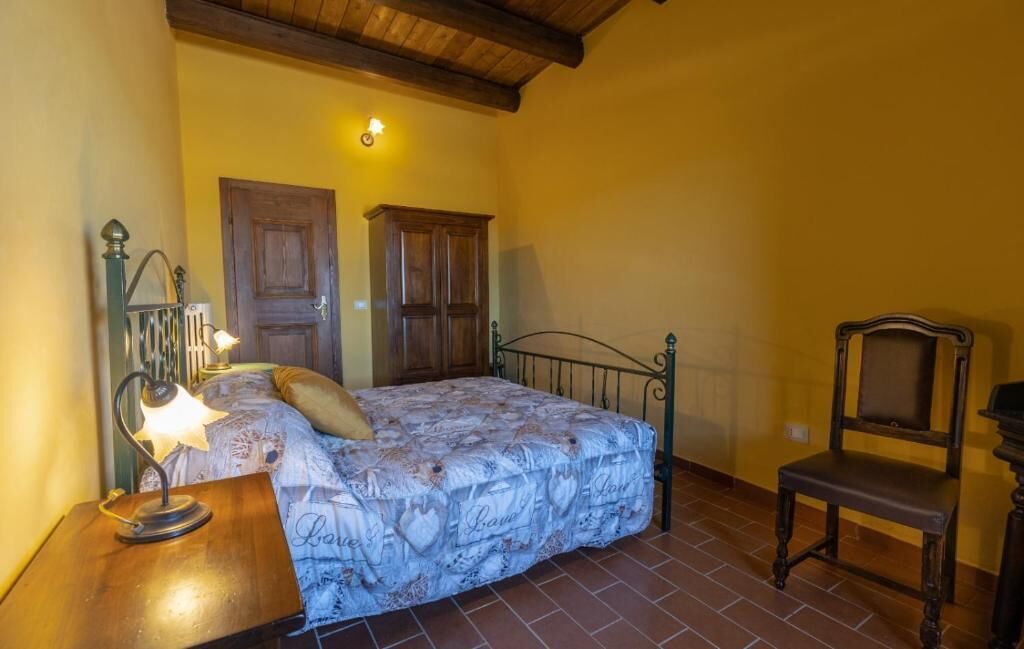 A bedroom with a bed, a nightstand, a chair, and a wooden door.