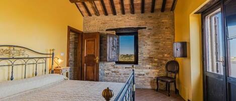 A bedroom with a bed, a stone wall, a wooden door, and a window.