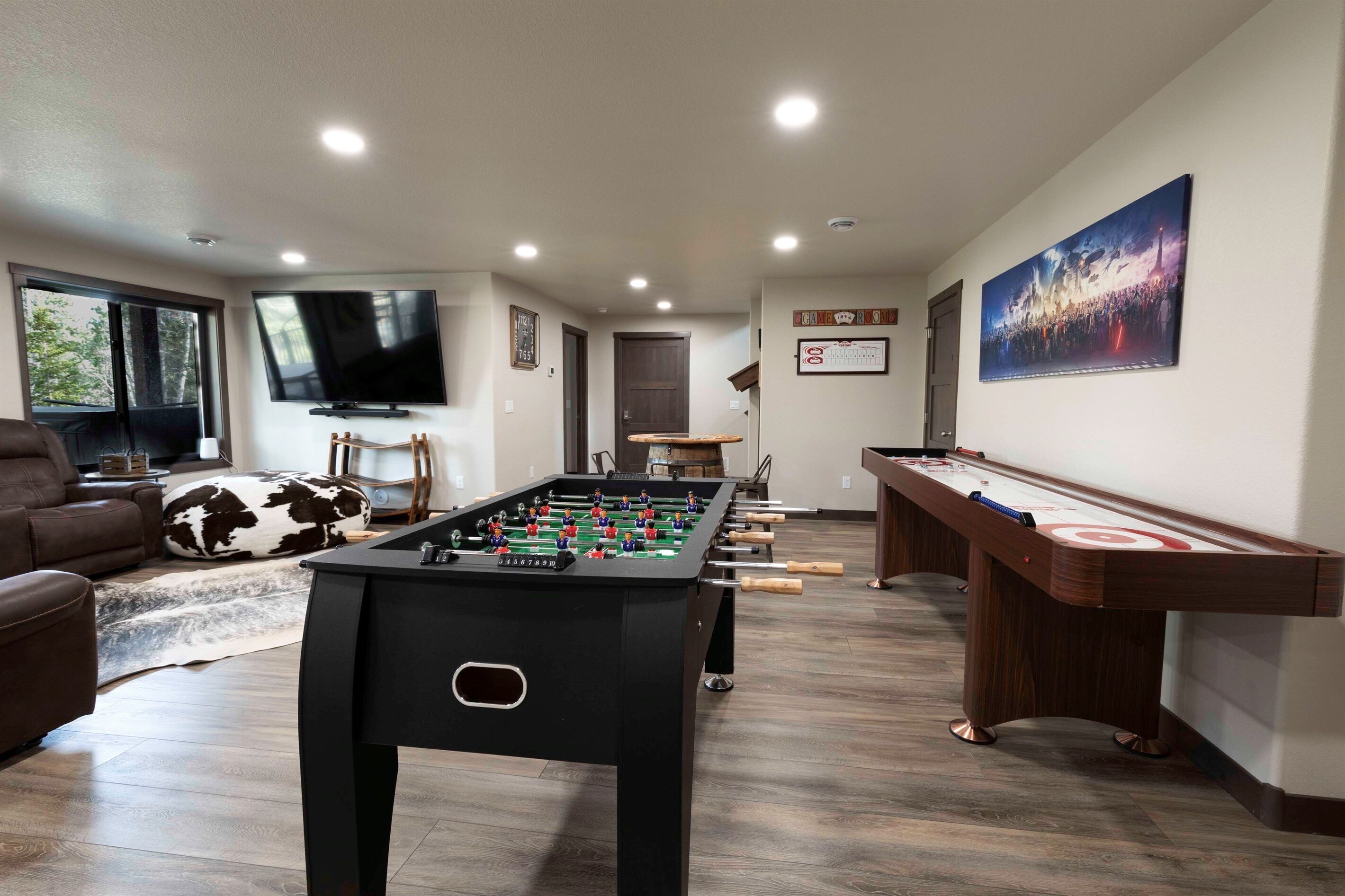 A living room with a foosball table, a pool table, a television, and a large window.