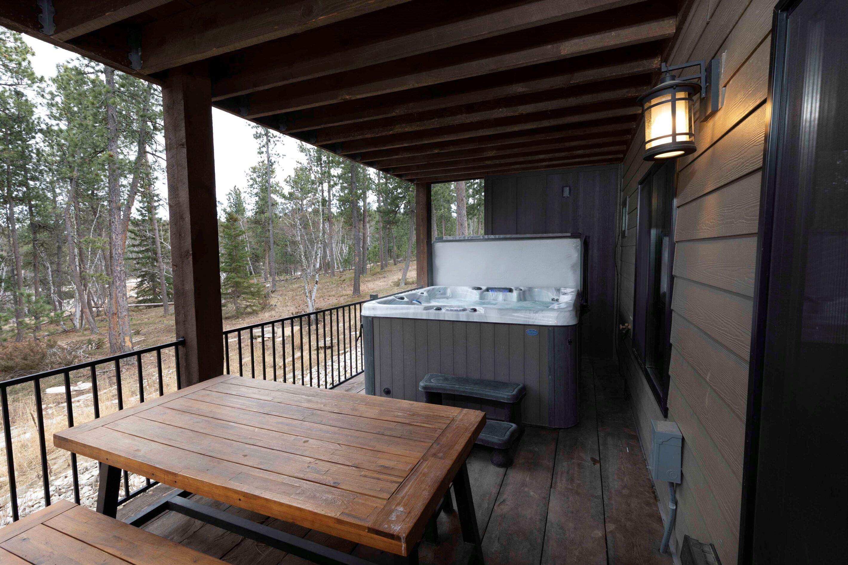 A wooden deck with a hot tub, a table, and a bench.