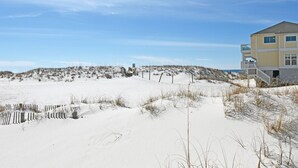 Una casa de playa con un paisaje arenoso, una cerca de madera y un cielo despejado.