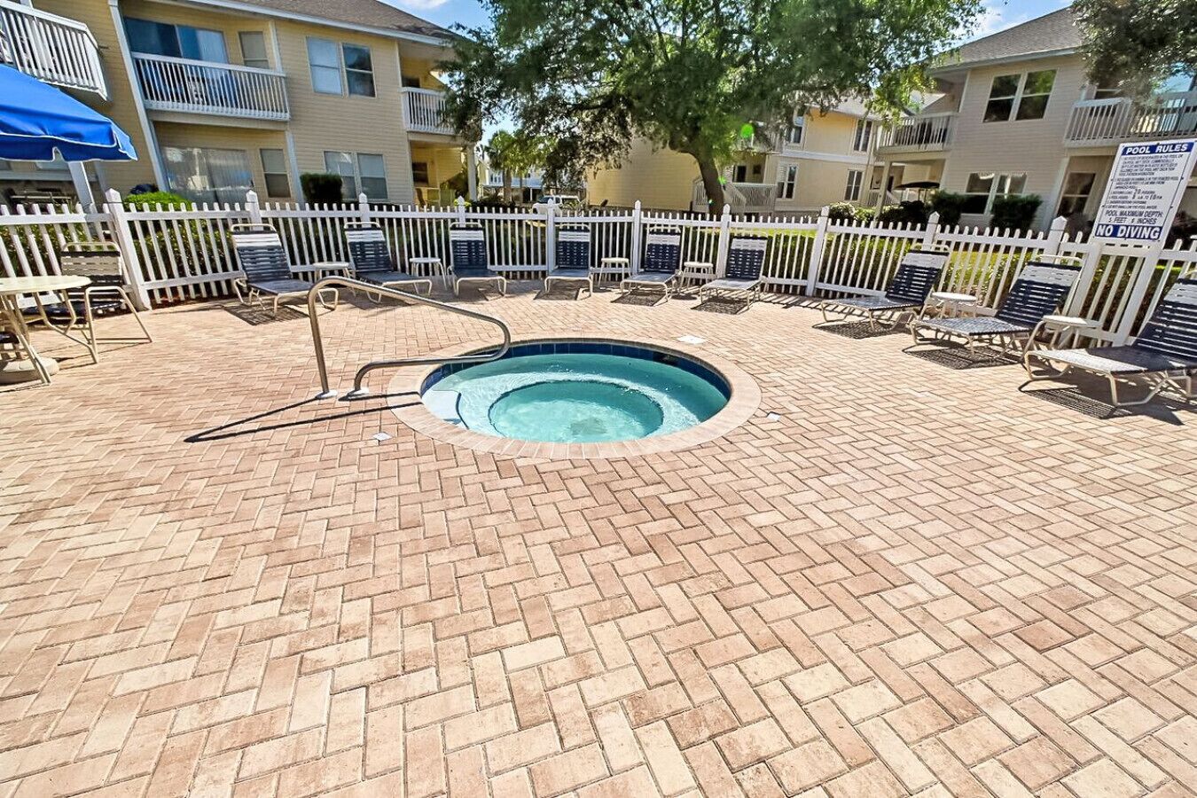 A brick-laid pool area with lounge chairs and a pool rule sign.