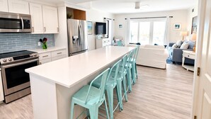 Una cocina moderna con electrodomésticos de acero inoxidable, una isla grande con taburetes de bar y una sala de estar con sofá y televisor.