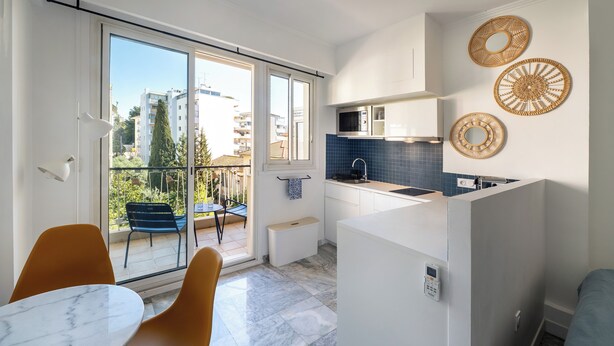 Une cuisine moderne avec une porte-fenêtre coulissante donnant sur un balcon, un petit coin repas avec une table en marbre et des œuvres d’art décoratives sur les murs.