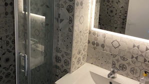 Une salle de bain avec des carreaux décorés, une cabine de douche en verre, un lavabo blanc et un miroir.
