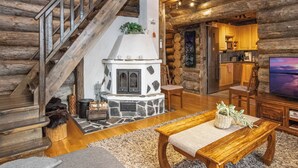 A log cabin interior with a stone fireplace, wooden staircase, and a kitchen area. - Villa kaunisvirta by Interhome (Pyhtää)