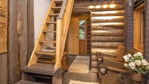 A log cabin interior with a wooden staircase, a cozy seating area with wicker furniture, and a small table with a vase of flowers. - Villa kaunisvirta by Interhome (Pyhtää)