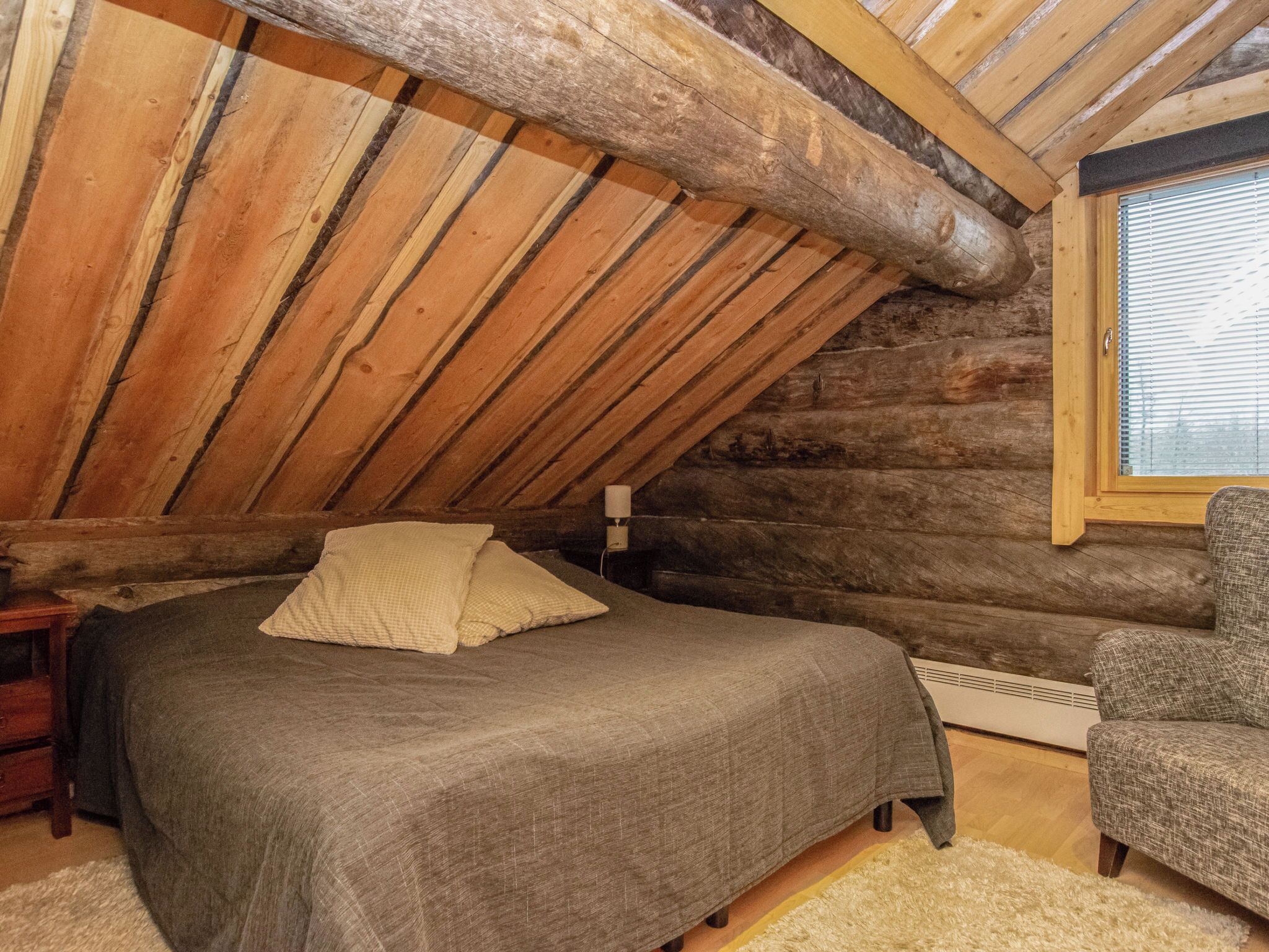Une chambre dans une cabane en rondins, avec un lit, une chaise et une fenêtre.