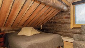 Une chambre dans une cabane en rondins, avec un lit, une chaise et une fenêtre.