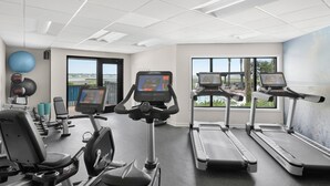 Ein Fitnessraum mit Laufbändern, Crosstrainern und Fahrrädern, mit großen Fenstern und Blick ins Freie.