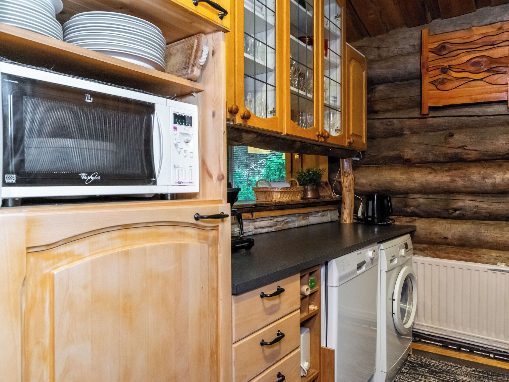 A kitchen with wooden cabinets, a microwave, a washing machine, and a wooden wall.