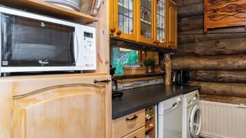 A kitchen with wooden cabinets, a microwave, a washing machine, and a wooden wall.