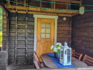 A wooden cabin with a wooden door, a ladder, a table with chairs, and a lantern.