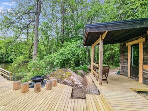 A wooden deck with a covered seating area, a grill, and a view of a forested area with a body of water.