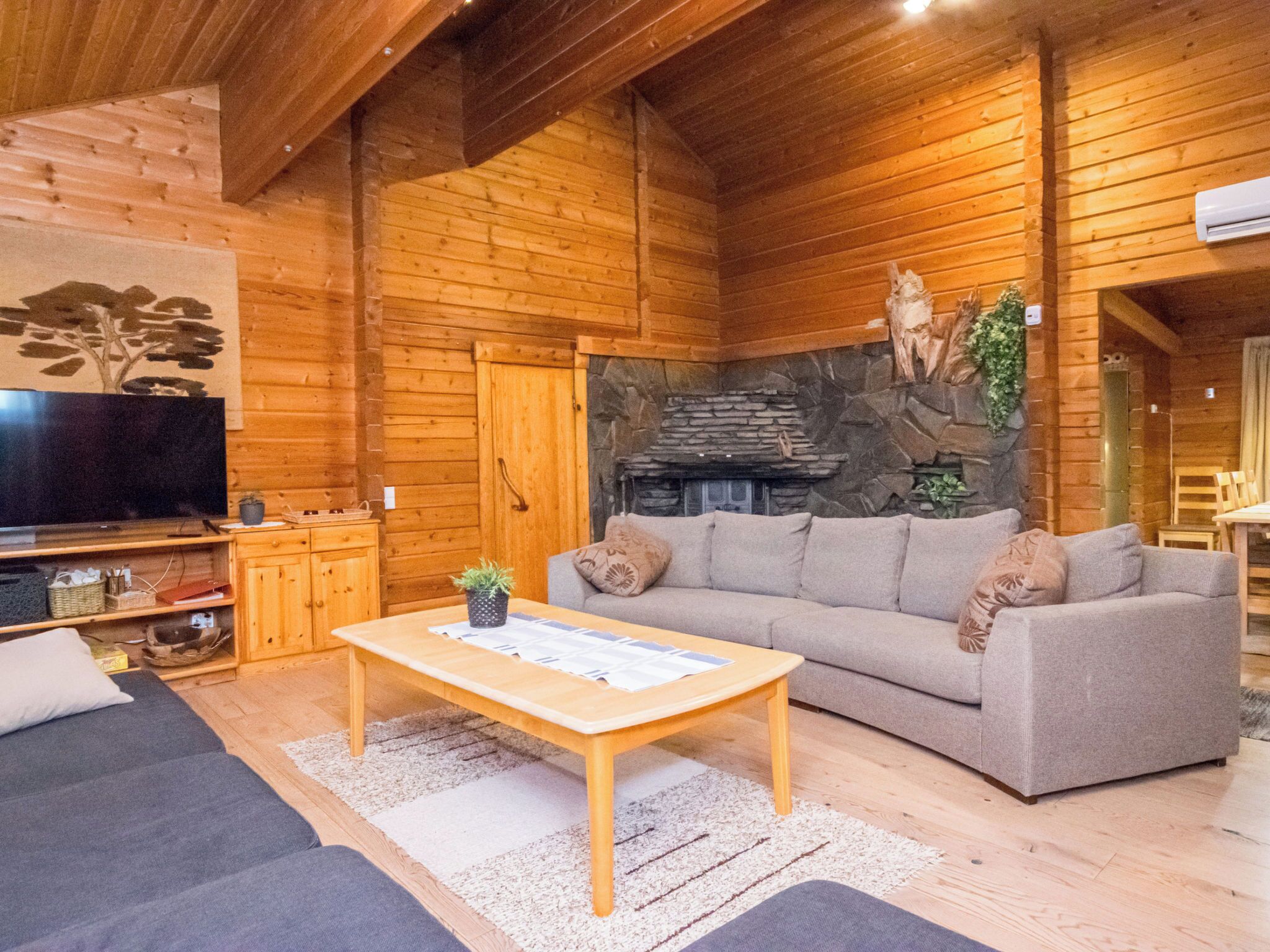 L’intérieur d’une cabane en rondins, avec une cheminée en pierre, un canapé, une table basse et un téléviseur.
