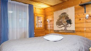Ein Schlafzimmer einer Holzhütte mit einem Bett, einem Fenster mit Vorhängen, einer Wandlampe und einer Wandteppich.