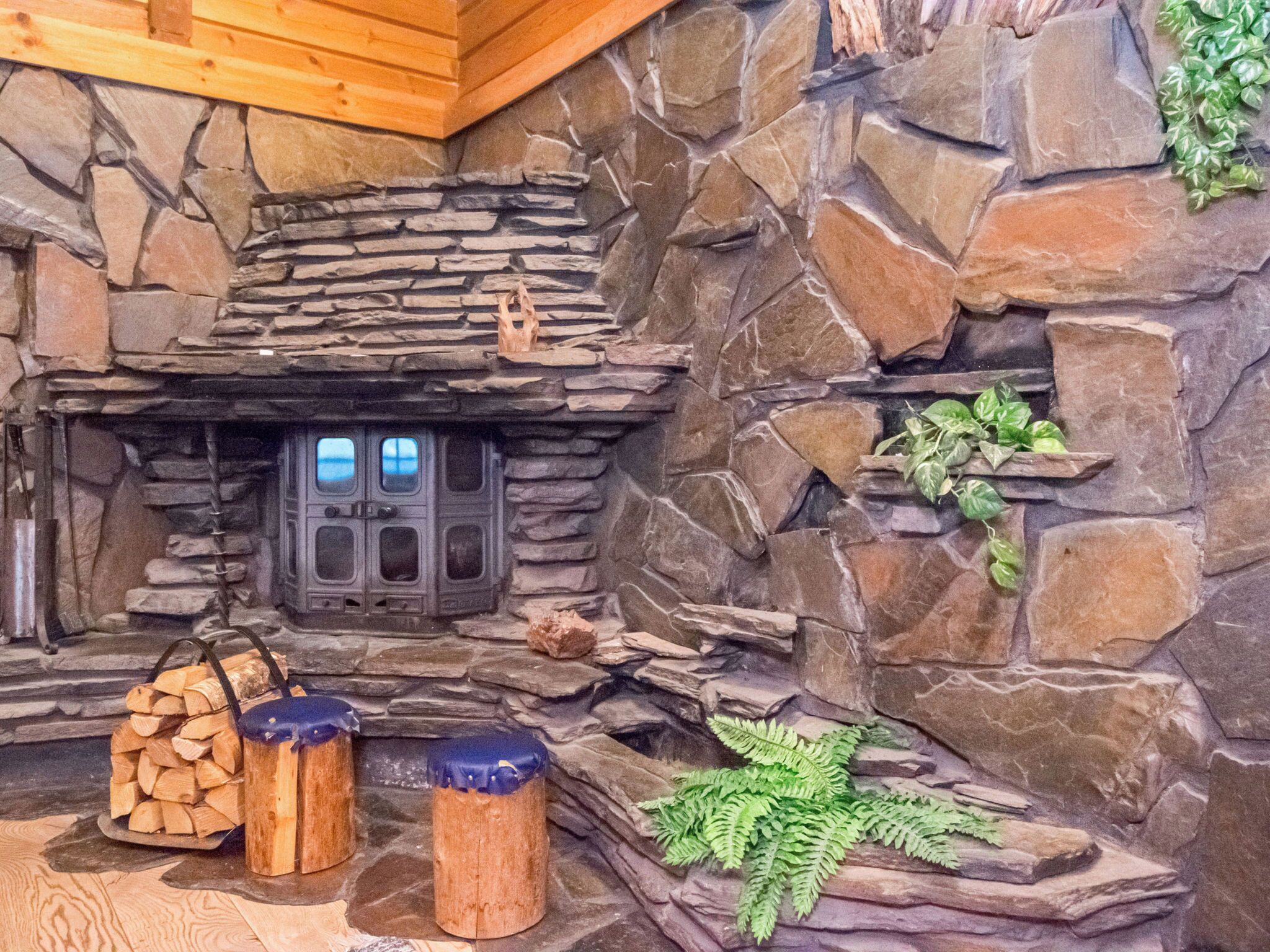A rustic stone fireplace with a wooden mantel, a set of stools, and a fern plant.