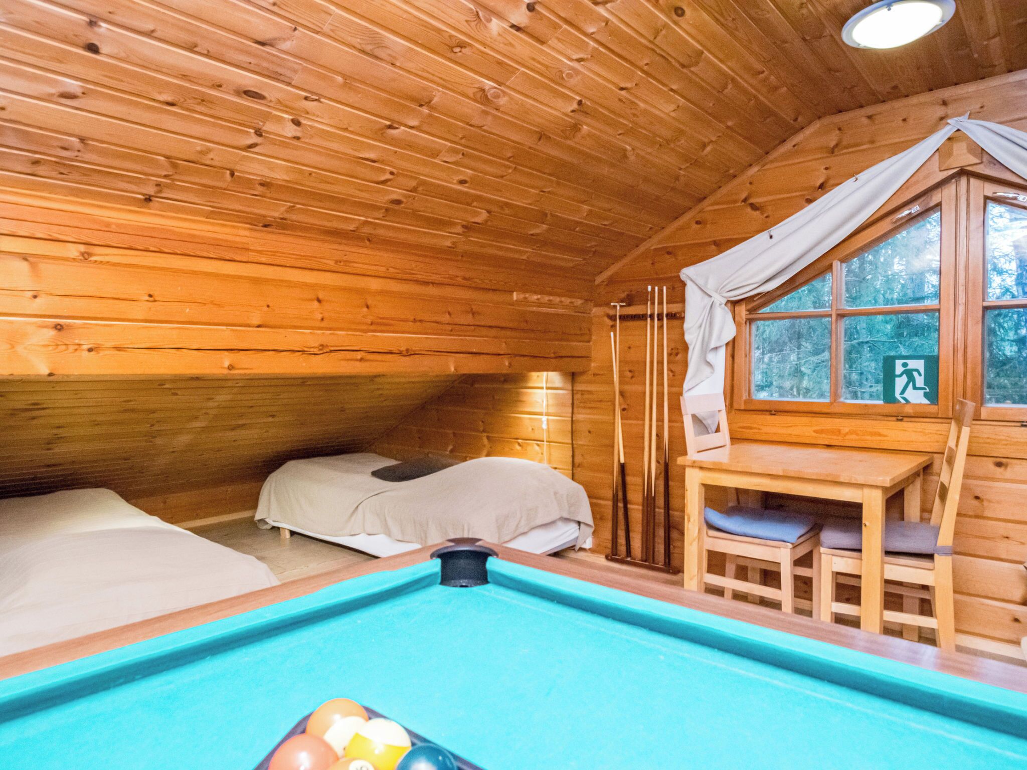 A wooden cabin with a pool table, a bed, and a window overlooking a forest.