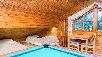 A wooden cabin with a pool table, a bed, and a window overlooking a forest.