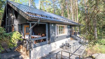 Eine Hütte mit einer Terrasse, Sitzgelegenheiten im Freien und Blick auf den umliegenden Wald.