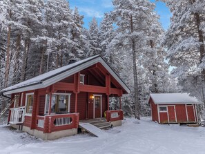 Een rode houten blokhut met een veranda, omringd door met sneeuw bedekte bomen.