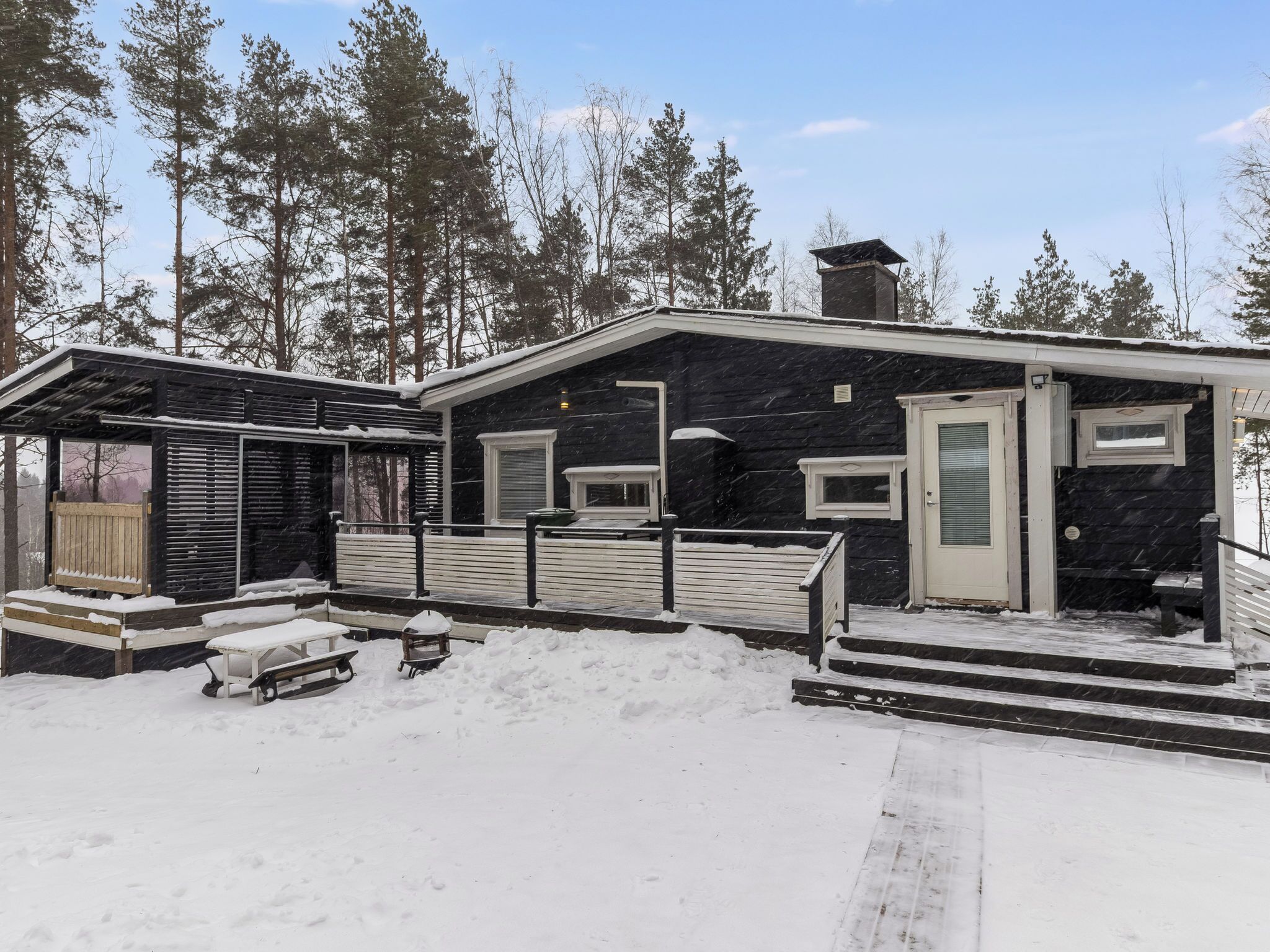 En stuga med en veranda, ett litet förråd och ett trädäck.