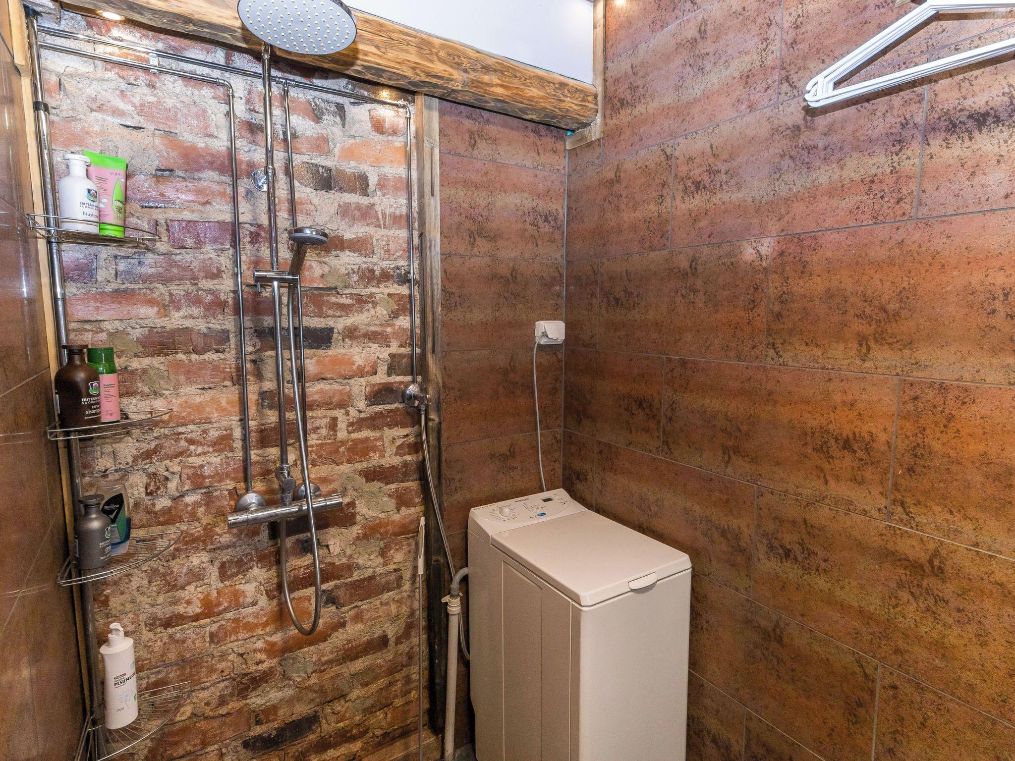 A shower with a brick wall, a metal showerhead, and a white washing machine.
