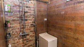 A shower with a brick wall, a metal showerhead, and a white washing machine.