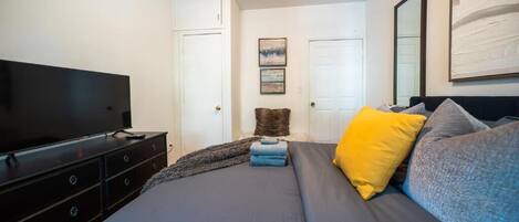 Un dormitorio con cama, televisor, cómoda y puerta.
