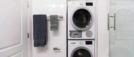 Un lavadero pequeño con lavadora Bosch, secadora y cabina de ducha de vidrio.