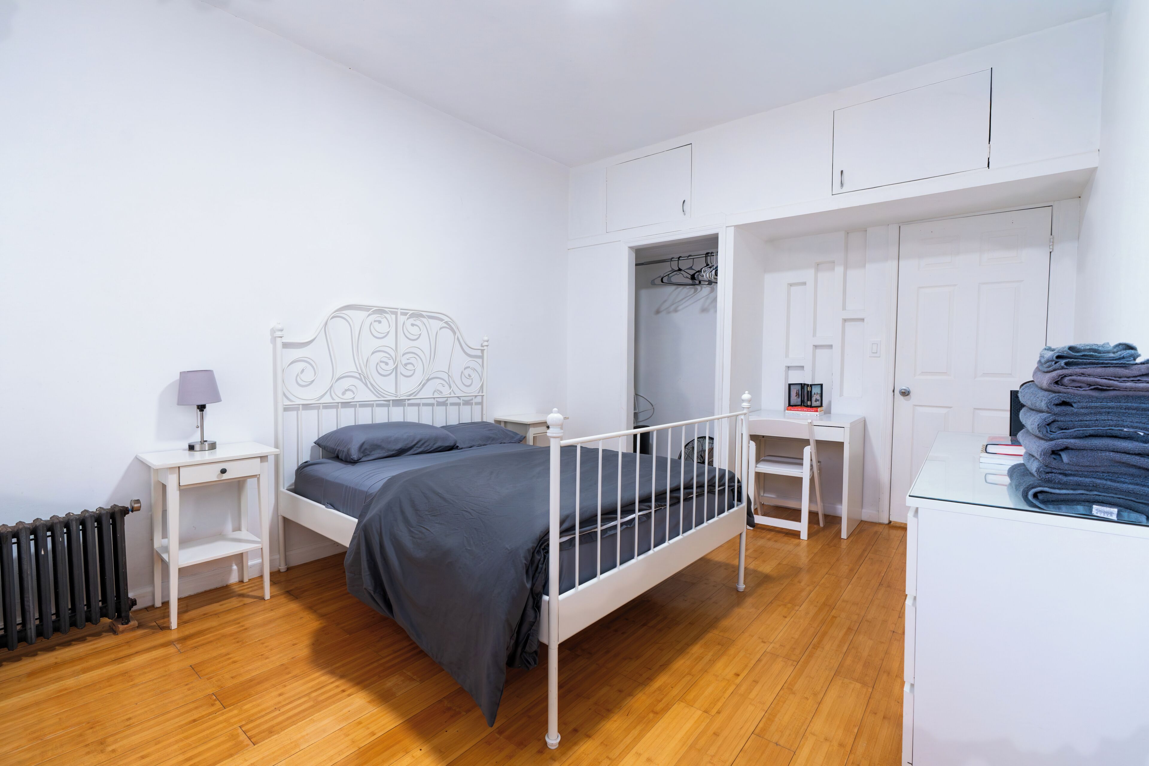 Une chambre à coucher avec un lit en métal blanc, une table de chevet avec une lampe, une armoire et un radiateur.