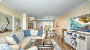 A living room with a sectional sofa, a dining area with a table and chairs, a TV on a stand, and artwork on the walls. - 2 Bedroom beach/pool view,37ft balcony, boat slip,6 month rental only, May-Oct. (Marco Island)