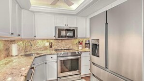A kitchen with white cabinets, a stainless steel refrigerator, a microwave, and a stove. - 2 Bedroom beach/pool view,37ft balcony, boat slip,6 month rental only, May-Oct. (Marco Island)