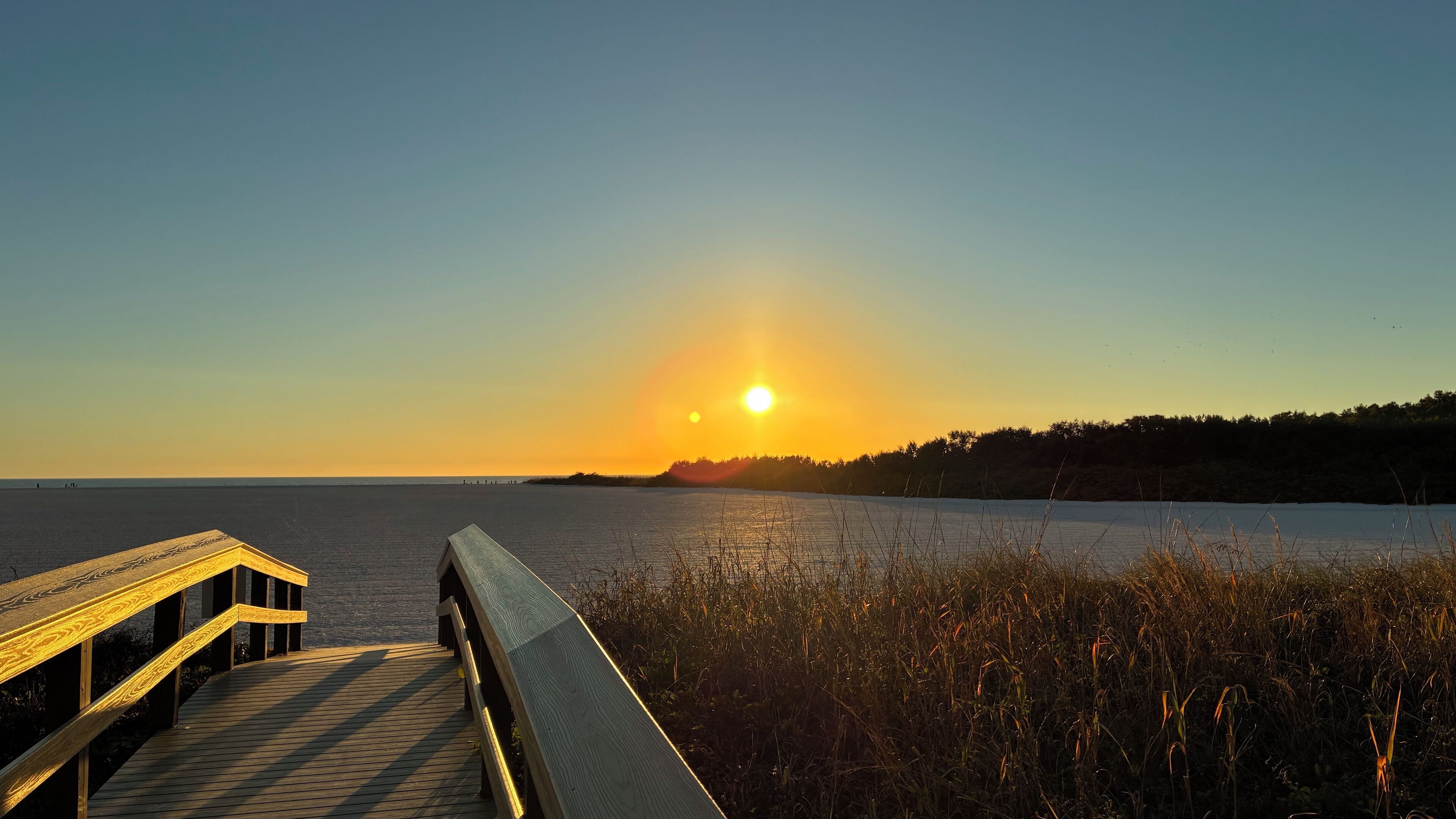A wooden pier extending into a body of water with a sunset in the background.