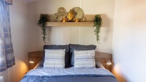 En säng med två kuddar, en sänggavel med dekorativa föremål och sänglampor.